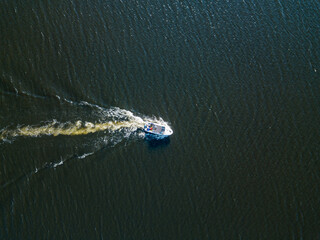 Aerial drone view. The motor boat is sailing along the river. Sunny summer day, small waves.