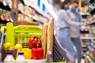 Young couple in masks shopping in supermarket