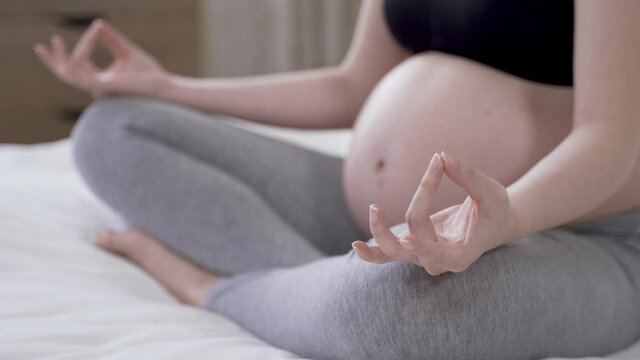 close up focus on mudra gesture with a pregnant woman performing yoga lotus pose at home.