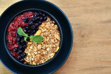 Top view, Granola with Berries in a black plate on wooden table.