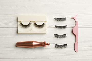 Flat lay composition with magnetic eyelashes and accessories on white wooden table