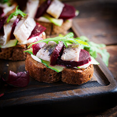 Herring fillet. Sandwich with salted herring and slice beetroot on the  toasts on wooden cutting board. Scandinavian cuisine.
