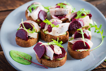 Herring fillet. Sandwich with salted herring and slice beetroot on the  toasts on wooden table. Scandinavian cuisine.