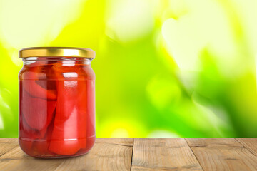 Jar of pickled bell peppers on wooden table against blurred background, space for text