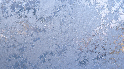 Ice and frost on the window pane in winter. Light blue backdrop. Frozen water crystal pattern...