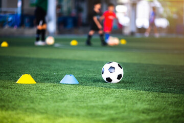 Selective focus to football with blurry marker cones on green artificial turf. Soccer equipment in soccer academy.
