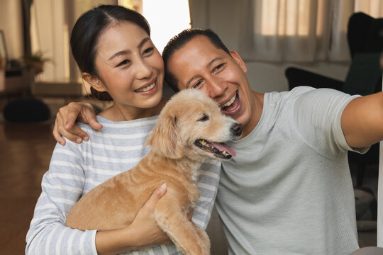 Portrait of an Asian and European couple hugging a dog for a selfie with their mobile phone. A young video conference call to father and mother. face time concept