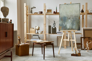 Unique artist workspace interior with stylish teak commode, wooden easel, bookcase, artworks, painting accessories, decoration and elegant personal stuff. Modern work room for artist. Template. - obrazy, fototapety, plakaty