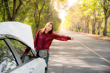 An Asian woman is waving and signaling a hand for help. Because her car is broken