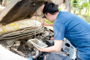 An Asian man tries to fix his car by checking the information on a tablet.
