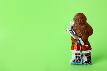 Sweet chocolate Santa Claus candy in slightly open foil wrapper on light green background, space for text