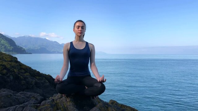 Girl Meditating at the Sea View. Meditation on the Rock. Young Woman Relaxing Alone in a Peaceful Place.