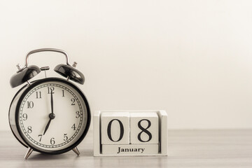 January 8 on a white calendar, next to a retro alarm clock on a light background.Calendar for January.Copy of the space.