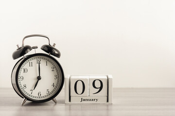 January 9 on a white calendar, next to a retro alarm clock on a light background.Calendar for January.Copy of the space.