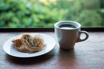 Hot coffee cup of americano, coffee with cookies in a dish on wooden table in the morning. mountain background