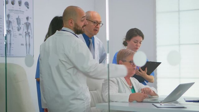 Senior doctor using laptop explaining to colleagues treatment of patients during medical brainstorming in meeting office on hospital. Medical team discussing diagnosis of issues record in workplace.