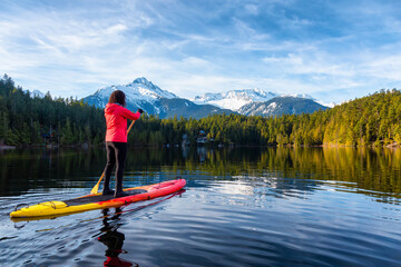 Adventurous Girl Paddle Boarding on Levette Lake with famous Tantalus Mountain Range in the background. Taken in Squamish, North of Vancouver, British Columbia, Canada.