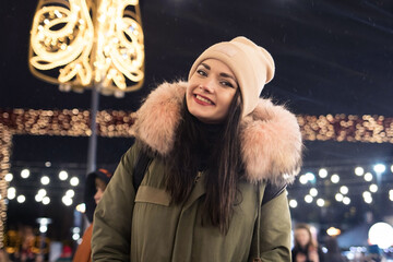 Night photo of the Christmas fair, a young girl against the background of Christmas tree lights