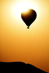 Silhouette of a rock and a balloon against the background of an orange sunset sky.