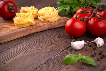Raw tagliatelle pasta with fresh basil, garlic and branch of tomatoes on rustic wooden table
