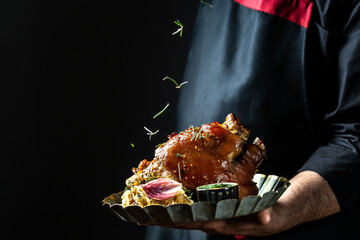 Chef hands cooking pork knuckle and adding fresh rosemary on black copy space background for menu restaurant or recipe text
