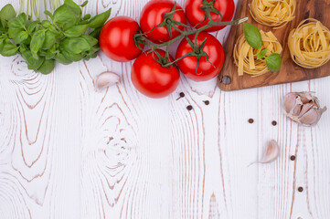 Top view raw tagliatelle pasta with fresh basil, garlic and tomatoes on a rustic white table, flat lay, copy space.