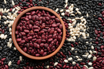 beans in brown ceramic bowl. bowl of beans. black bean, red kidney bean and white bean. navy bean, cannellini bean, white kidney bean on background made from beans and scattered various beans