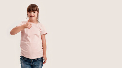 Portrait of disabled girl with Down syndrome smiling at camera, showing thumbs up with one hand...