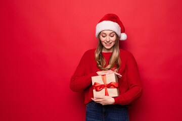 Beautiful lwoman in santa hat holding giftbox in hands isolated on red background