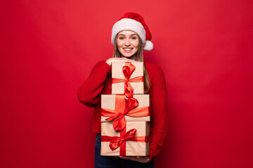 Excited surprised woman in red santa claus outfit holding stack presents isolated on the red background