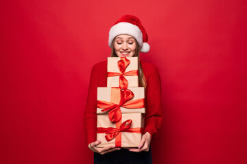 Excited surprised woman in red santa claus outfit holding stack presents isolated on the red background
