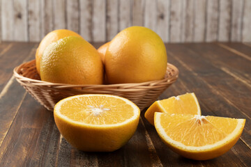 Oranges in a basket with cut fruits over wooden table