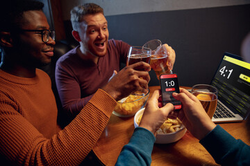 Clinking, winners. Excited fans in bar with beer and mobile app for betting, score on their...