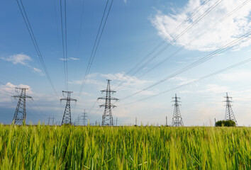 High voltage lines and power pylons and a green agricultural landscape on a sunny day.