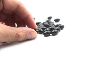 Obraz na płótnie Canvas Closeup of black pills of coal in hand on white background