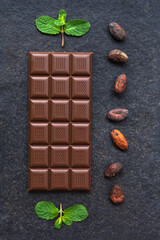 Milk chocolate with mint and cocoa beans on a black stone background