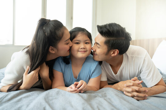 happy asian family in the bedroom.young asian parents kissing their daughter while lying on bed.