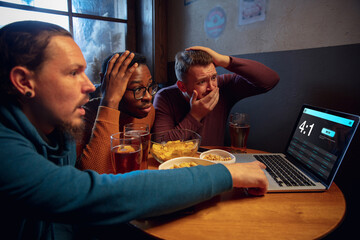 Shocked. Excited fans in bar with beer and mobile app for betting, score on their devices. Screen with match results, emotional friends cheering. Gambling, sport, finance, modern techn concept.