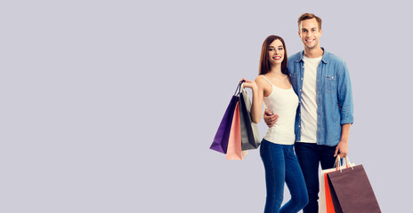 Love, holiday sales, shop, retail, consumer concept - happy embracing couple with shopping bags. Isolated over grey color background. Studio shot.