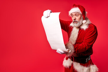 santa claus surprisingly read Merry Christmas wish list paper roll, he is in shock by wishes, wearing santa suit and hat, isolated portrait