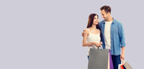Love, holiday sales, shop, retail, consumer concept - happy embracing couple with shopping bags, looking at each other. Grey background. Copy space for text.