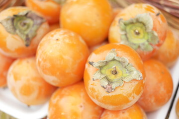 Heap of persimmon fruits close up. Pile of tasty tropical fruits at street market. Rich with vitamins.
