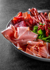 plate with meat, salami, ham, backon, prosciutto on Dark grey black slate background