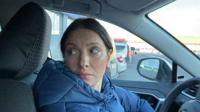 Woman driver driving car back into parking spot in the open parking lot of the supermarket