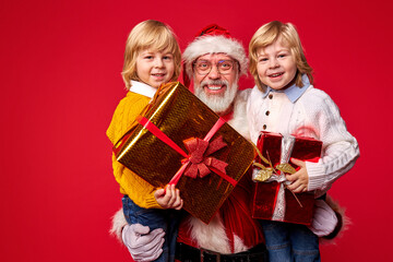 santa claus with children, senior santa congratulating kids with happy new year, x-mas, isolated on red background, kids holding gift boxes