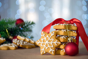 Stack of traditional Christmas gingerbread in star shape with red ribbon and toy with holidays decor and bokeh lights on background. New Year and Christmas celebration. Homemade festive cookies.