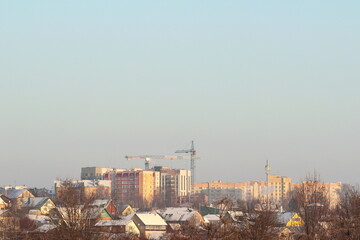 New modern multi-storey houses against the backdrop of small village houses on a clear winter day.