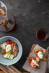 morning eating concept Breakfast assortment with waffles, egg vegetable bowl and coffee on black background