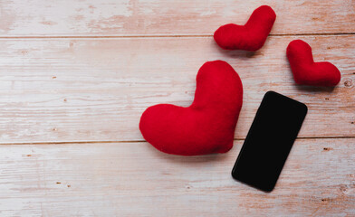 Online greetings and correspondence for Valentines day on February 14. Empty space for text or design, receive and give gifts phone. Valentines day smartphone on wooden table next to red toy hearts.