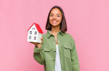 young hispanic woman smiling happily with a hand on hip and confident, positive, proud and friendly...
